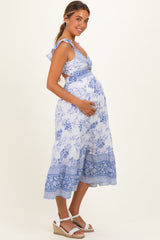 woman wearing a blue and white floral maternity dress with ruffle straps, cradling her baby bump