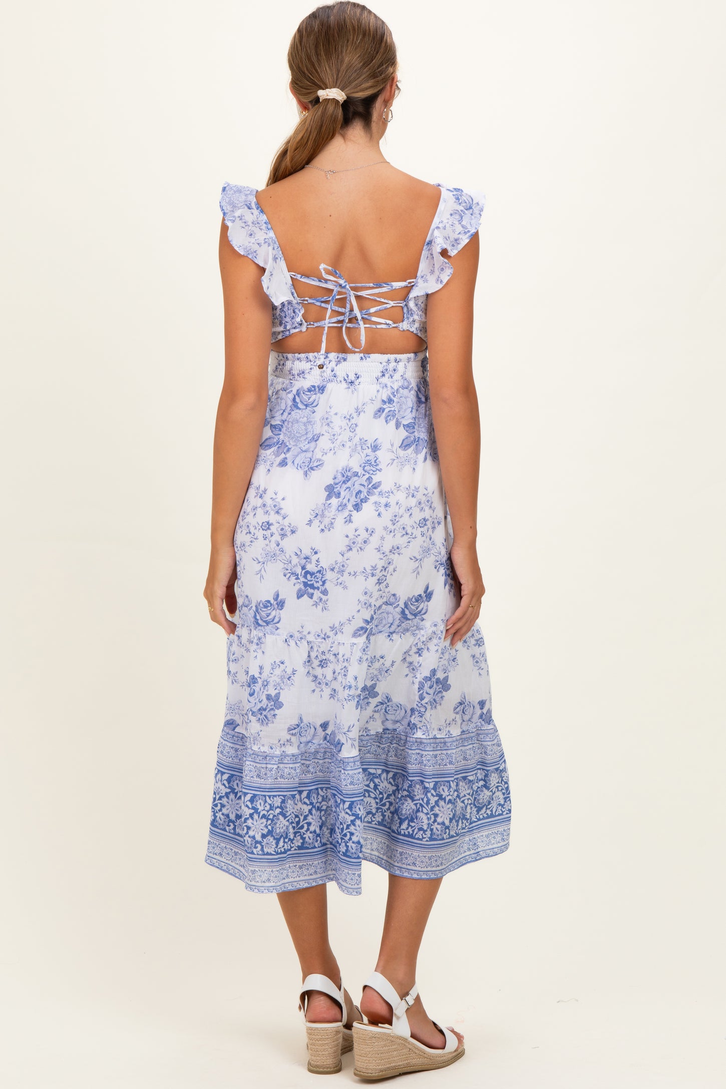 woman wearing a blue floral maternity dress with ruffle straps and a lace-up back detail