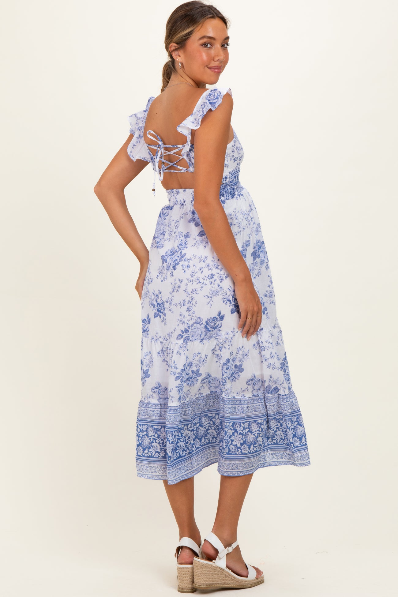 woman wearing a blue and white floral maternity dress with ruffled straps and a lace-up back, showing her baby bump