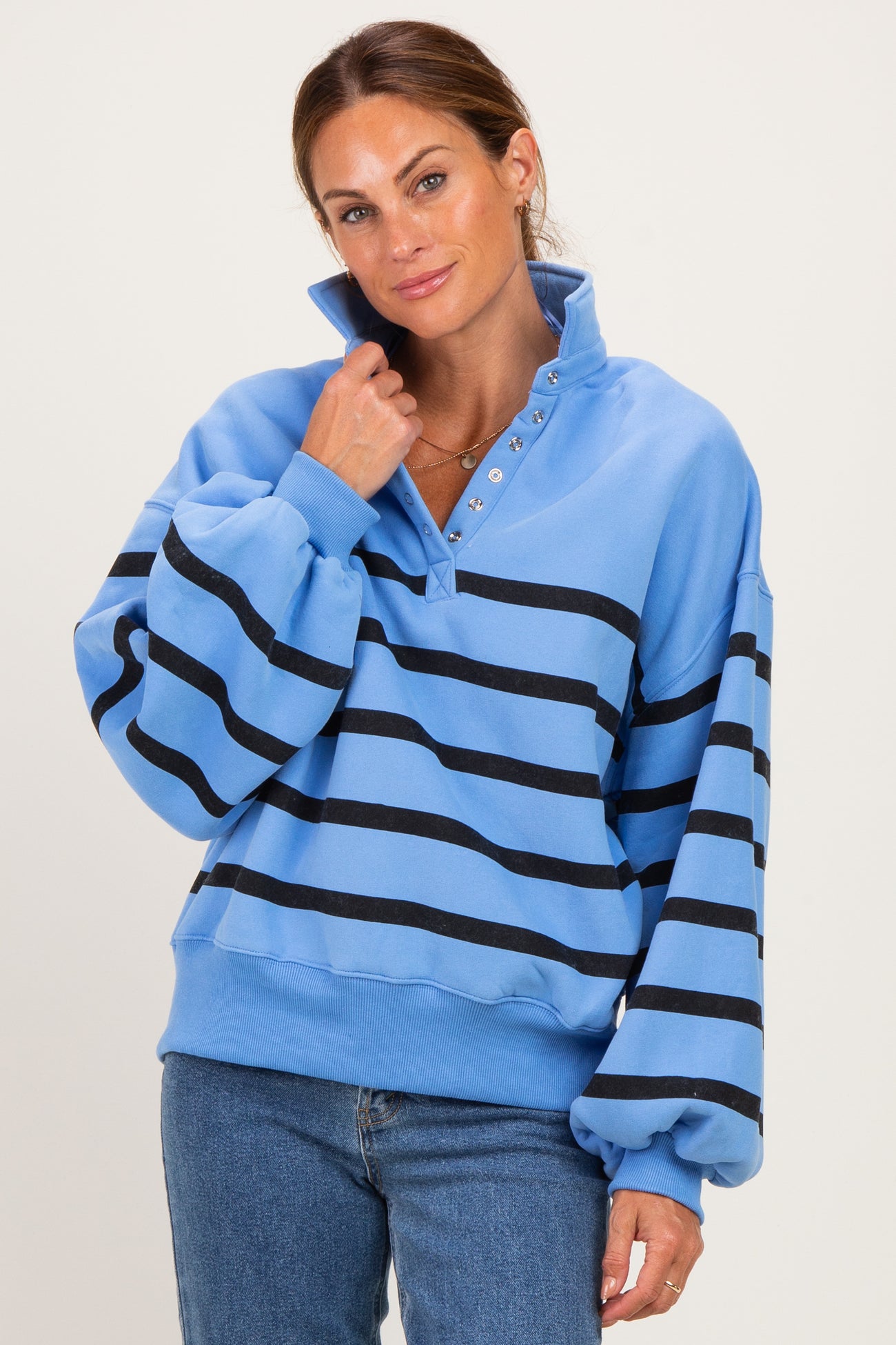 woman wearing a light blue oversized pullover with black stripes and snap-button collar paired with blue jeans