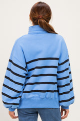 woman wearing a blue striped pullover sweatshirt with oversized sleeves and a high collar, viewed from the back