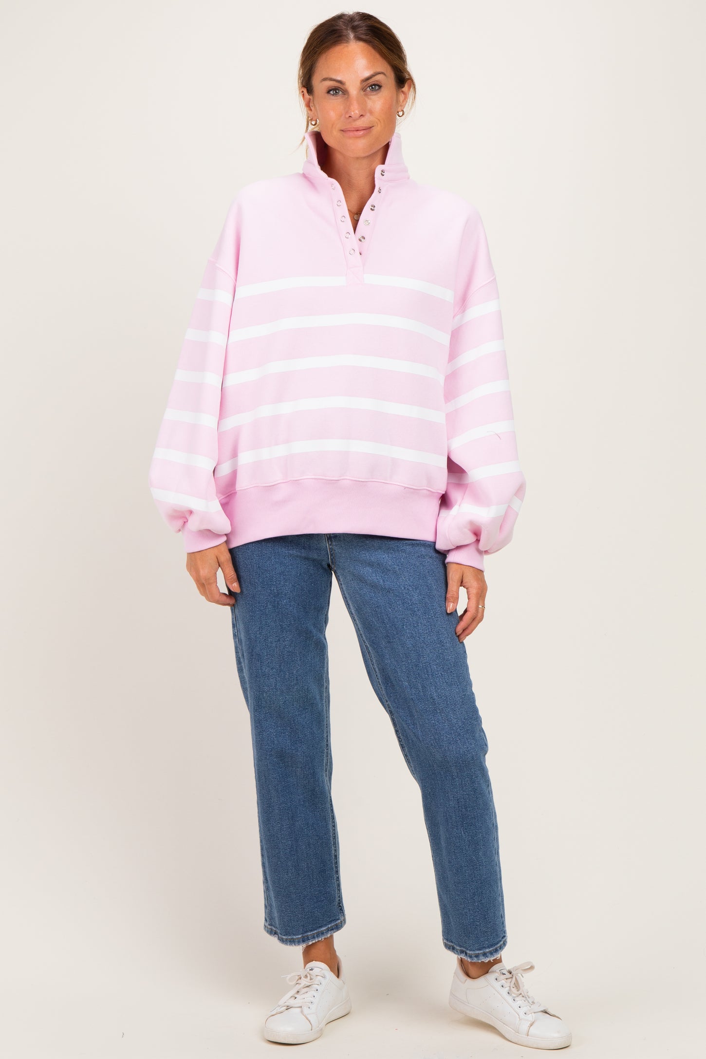 woman wearing a pink striped oversized pullover sweatshirt with a quarter zip and relaxed fit jeans