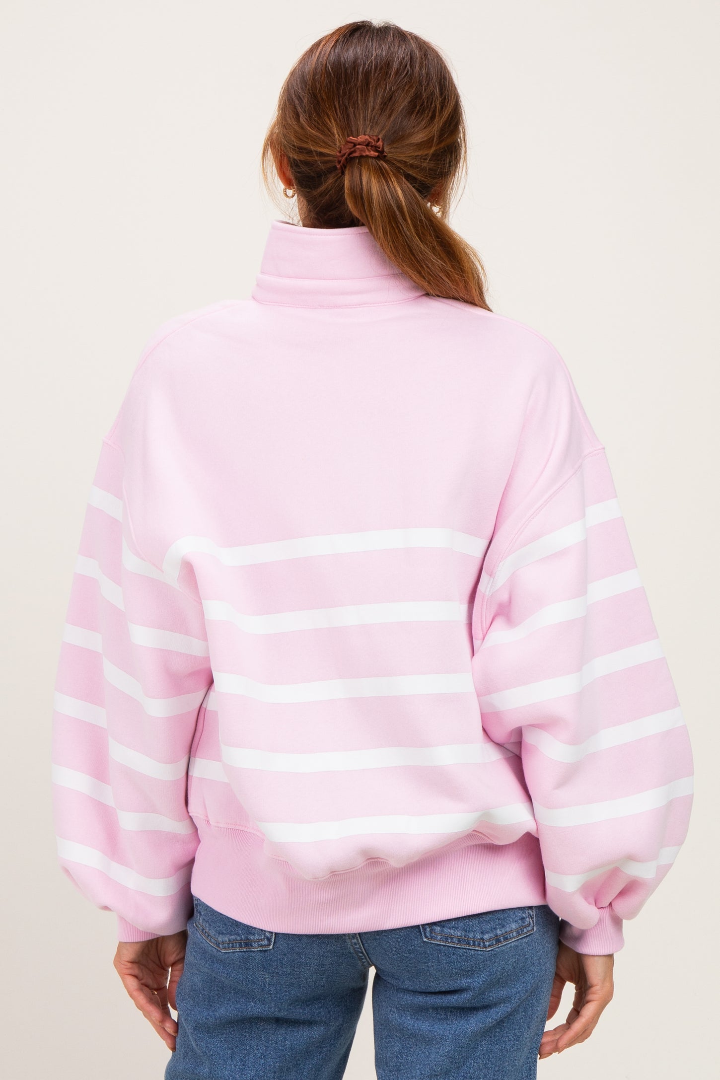 woman wearing a pink and white striped oversized sweatshirt with a high collar, viewed from the back