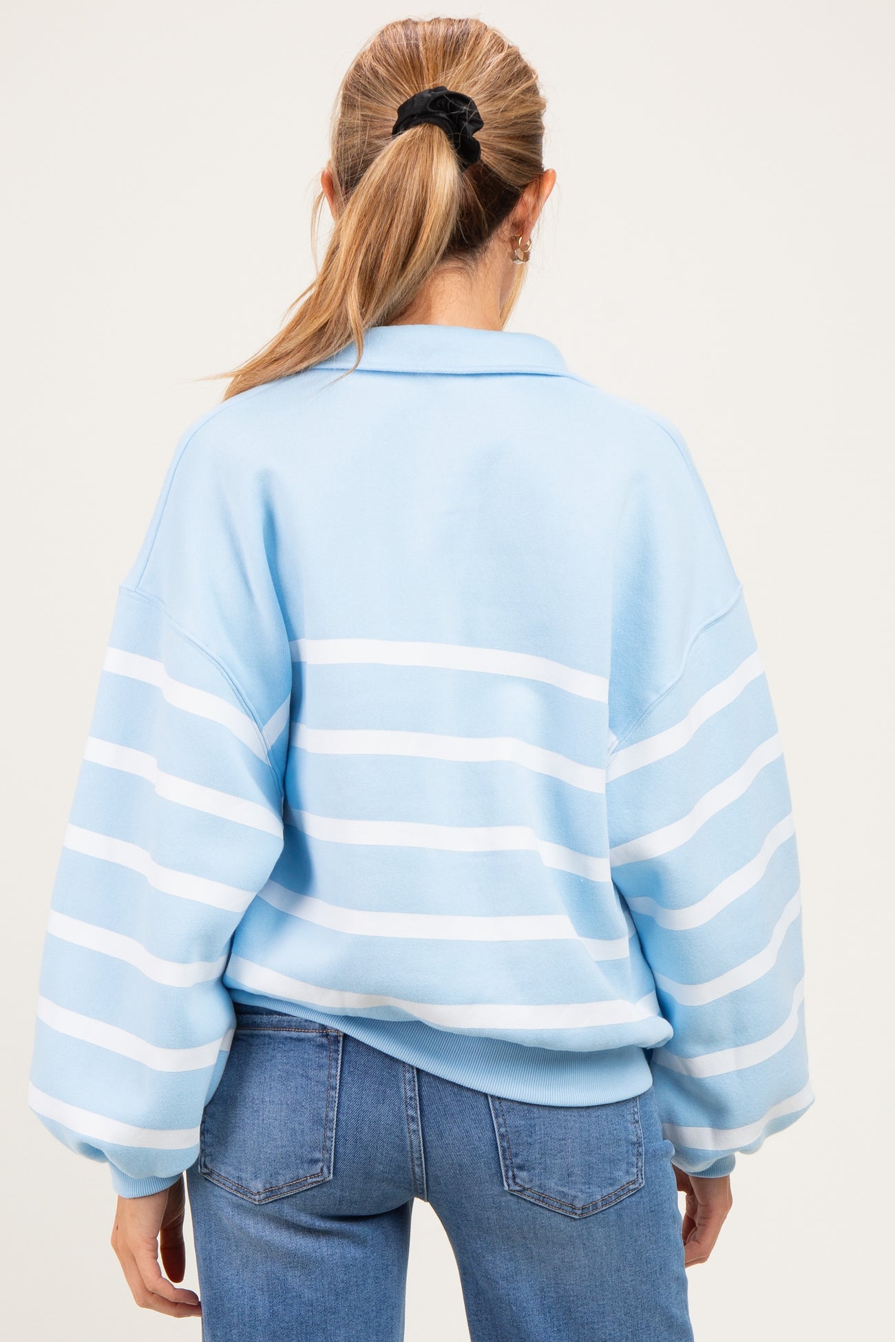 woman wearing a light blue striped oversized maternity sweatshirt with a polo collar, seen from the back