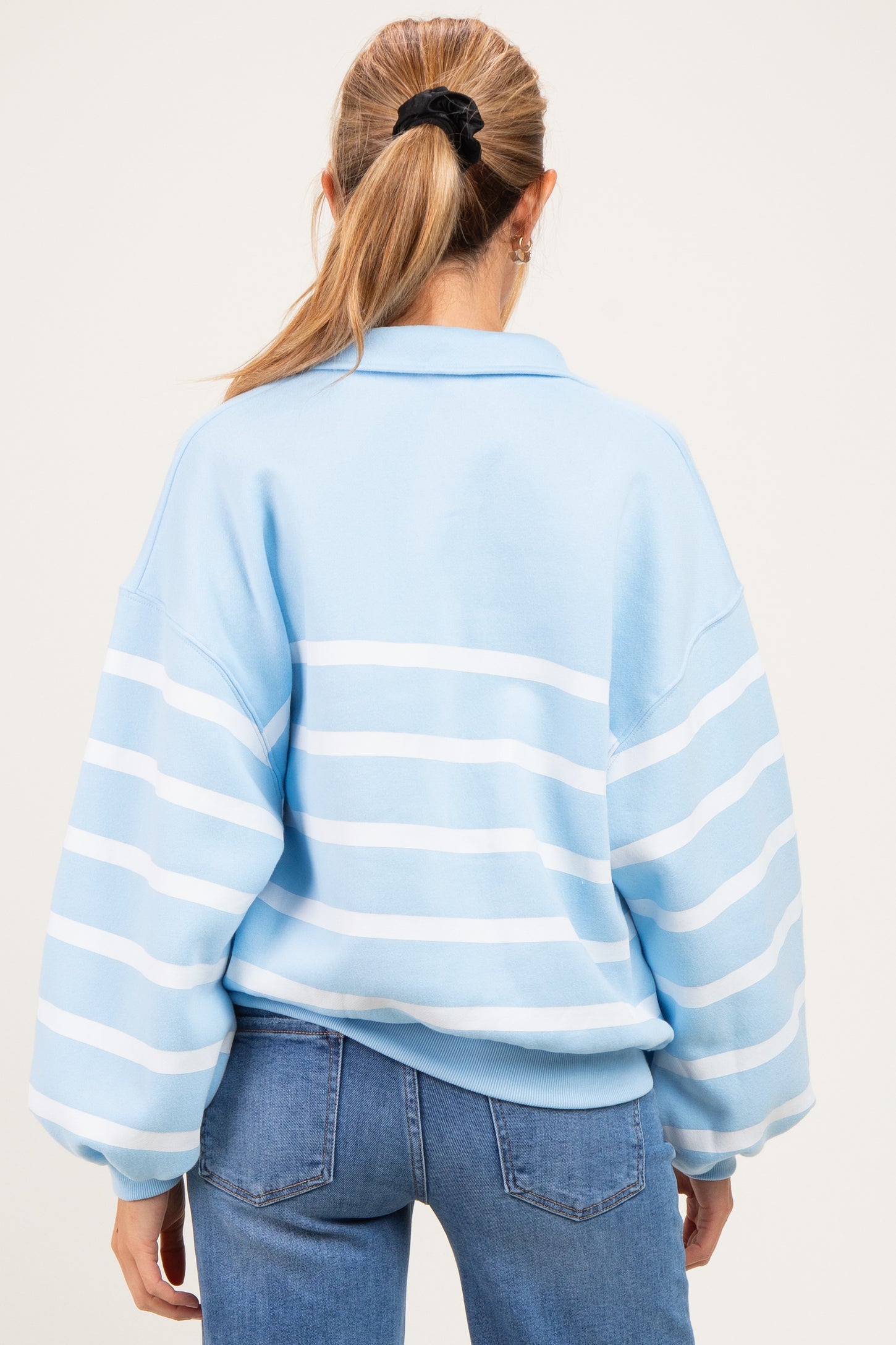 woman wearing a light blue striped oversized maternity sweatshirt with a polo collar, seen from the back