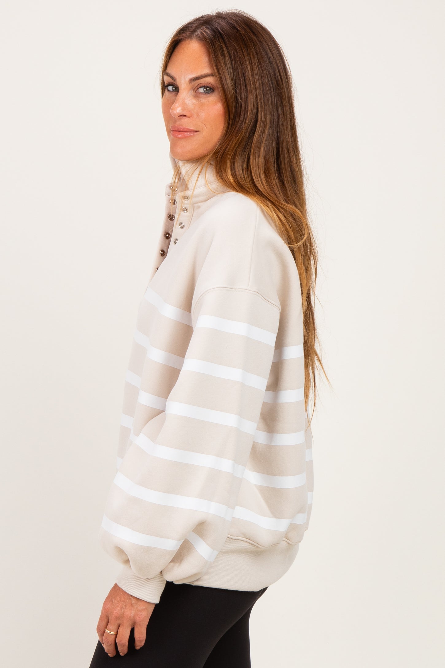 woman wearing a beige striped oversized sweatshirt with button detailing on the collar and black leggings