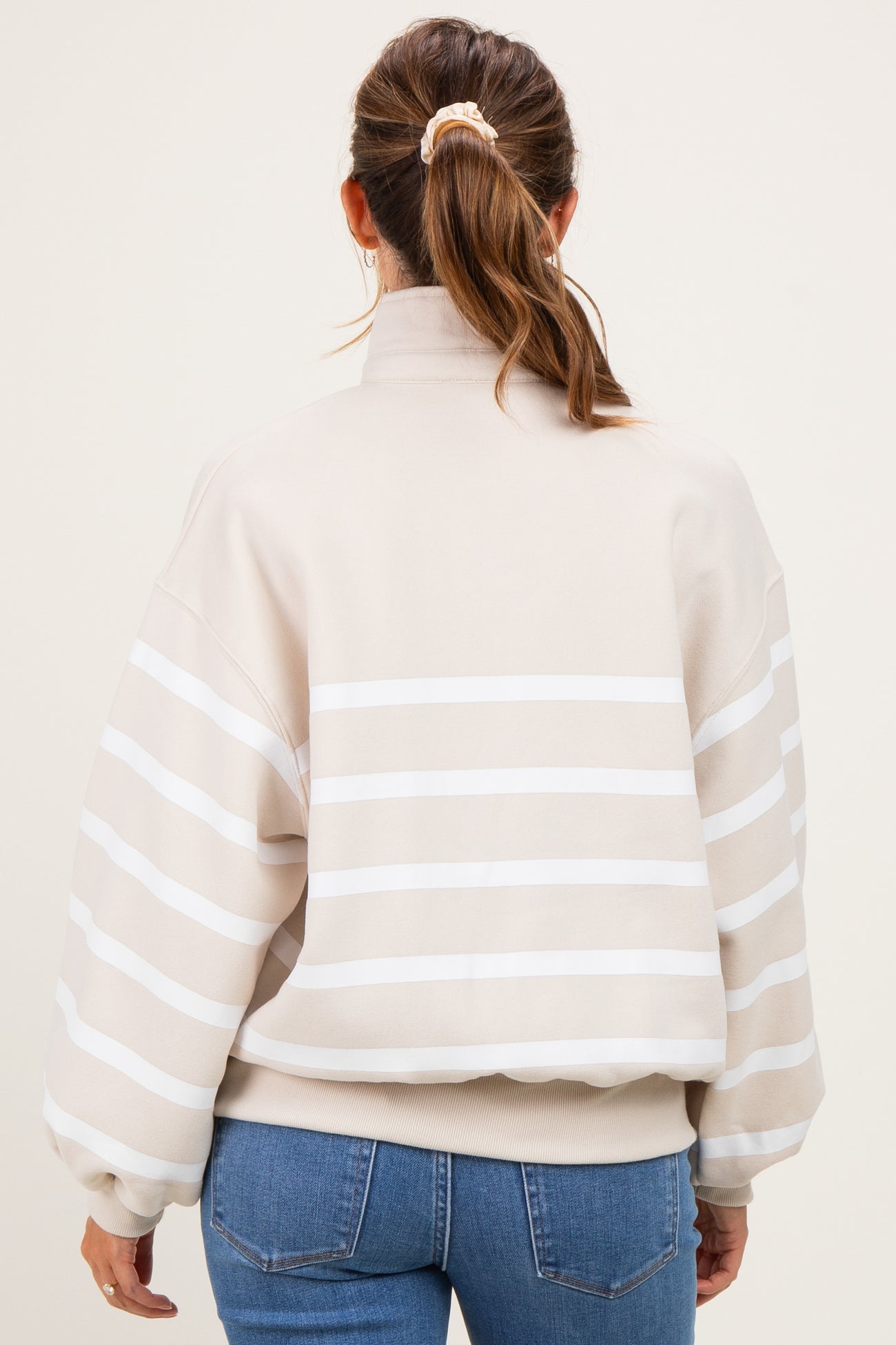 woman wearing a beige striped maternity sweatshirt with a high neck and balloon sleeves, seen from the back