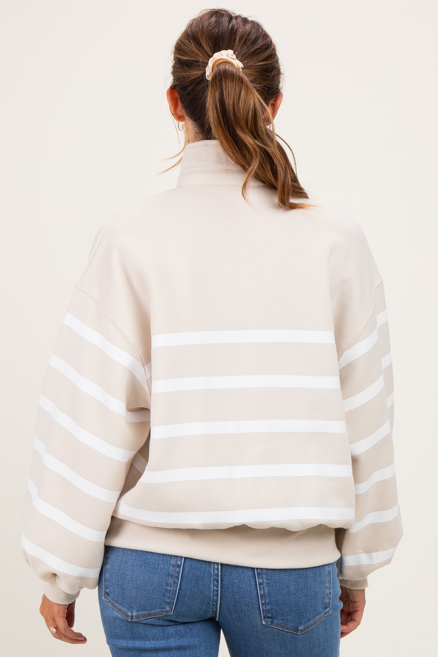 woman wearing a beige striped maternity sweatshirt with a high neck and balloon sleeves, seen from the back