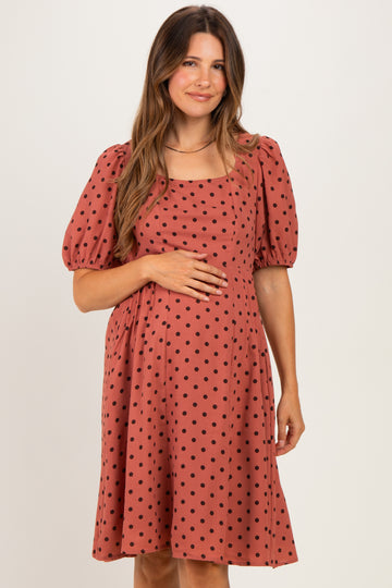 woman wearing a rust colored maternity dress with puff sleeves and black polka dots, holding her baby bump