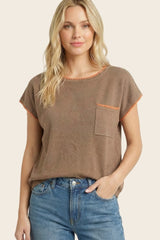 woman wearing a brown short sleeve top with orange trim and a front pocket, paired with blue jeans