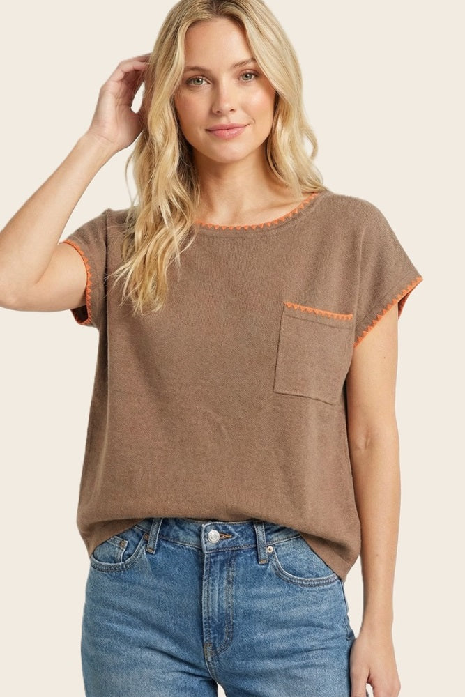 woman wearing a brown short sleeve top with orange trim and a chest pocket, styled with light blue high-waisted jeans
