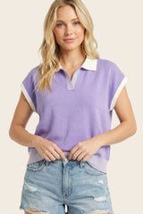 woman wearing a lavender short sleeve polo top with white collar and striped hem, paired with denim shorts