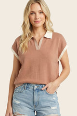 woman wearing a rust-colored short sleeve top with a collared neckline and striped details, paired with distressed denim shorts