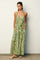 woman wearing a green palm leaf patterned maxi dress with a v-neckline and adjustable tie waist, standing against a wall