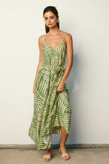 woman wearing a green leaf print maxi dress with spaghetti straps and a gathered waist, standing against a neutral wall