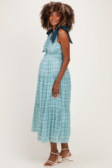 woman wearing a teal plaid maternity dress with tie straps and a visible baby bump