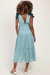 woman wearing a green and blue plaid maternity dress with a back tie detail and tiered skirt.