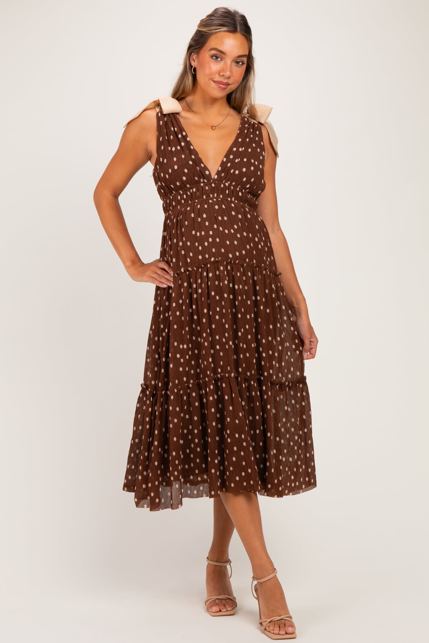 woman wearing a brown polka dot maternity dress with a v-neck and tiered skirt, showing off her baby bump