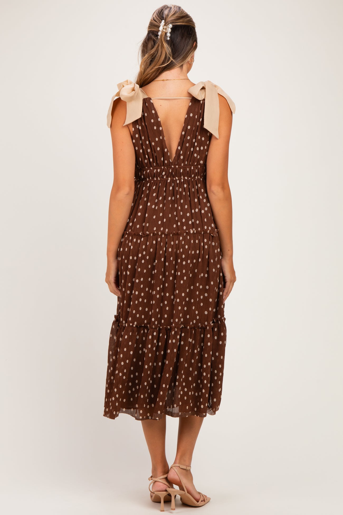 woman wearing a brown polka dot maternity dress with tie shoulder straps and a tiered skirt, revealing a baby bump from behind