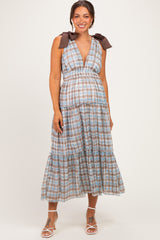 woman wearing a brown and blue checkered maternity dress with tied straps and a flowing midi skirt, highlighting her baby bump