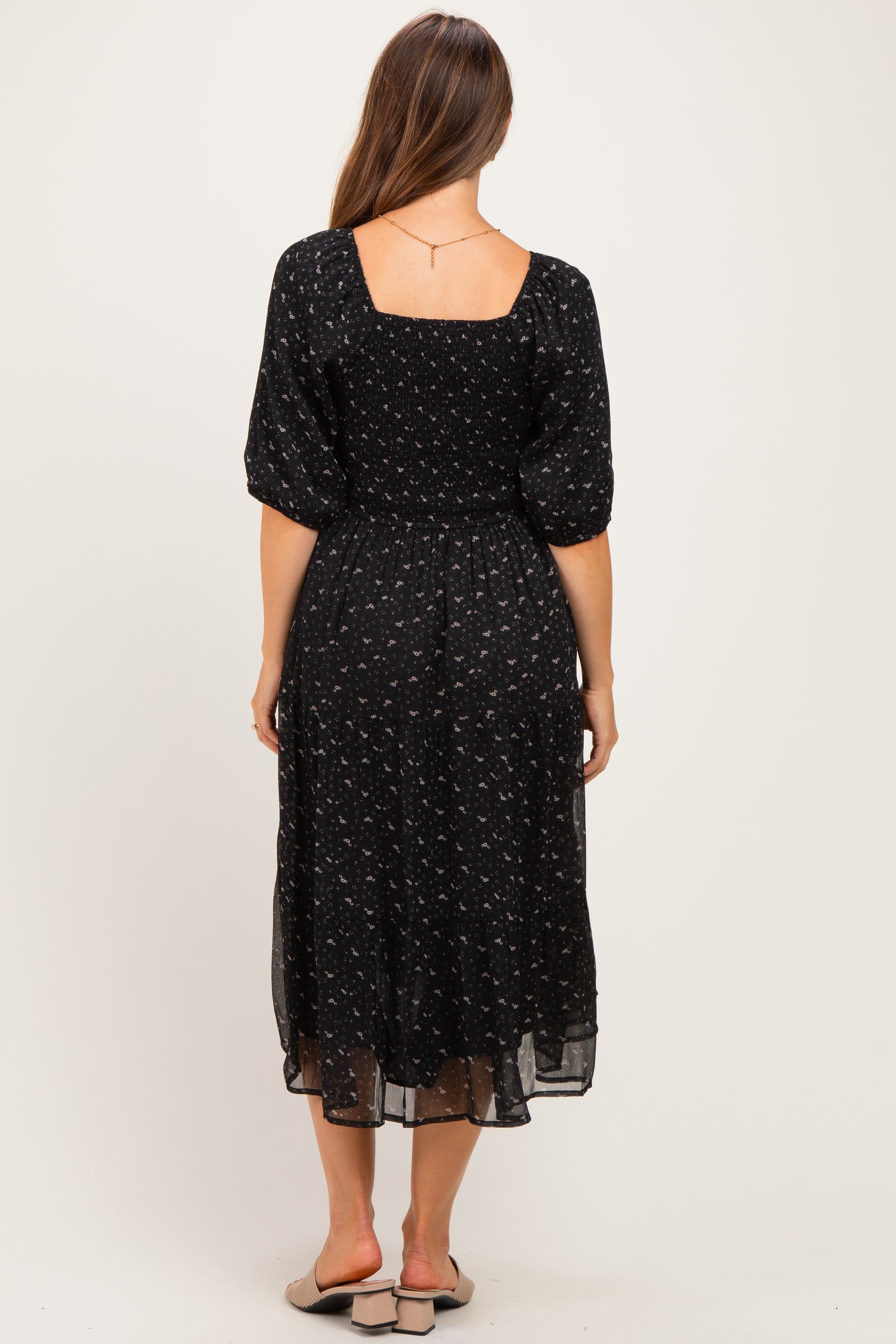 woman wearing a black floral maternity dress with a square neckline and puff sleeves, showing a baby bump