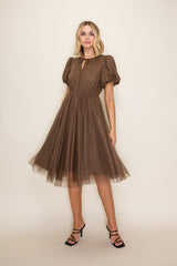 woman wearing a brown polka dot dress with puff sleeves and a keyhole neckline, standing against a neutral background