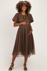 woman wearing a brown polka dot maternity dress with puff sleeves and a tie detail, gently holding her baby bump
