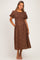woman wearing a brown floral print maternity dress with short puff sleeves and a smocked bodice, standing with hands in pockets