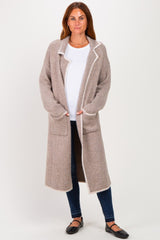woman wearing a long beige cardigan with white trim and pockets over a white shirt and blue jeans