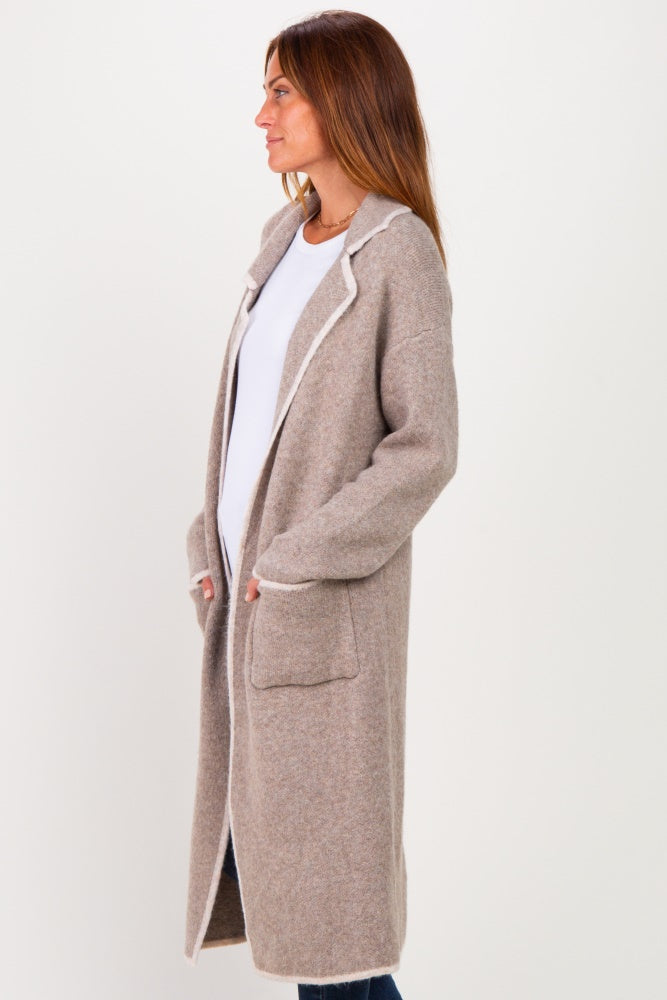 woman wearing a beige long sleeve cardigan with white trim and pockets, standing sideways against a light background