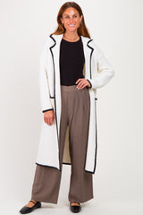 woman wearing a cream long cardigan with black trim, black fitted top, and wide-leg taupe pants, smiling at the camera