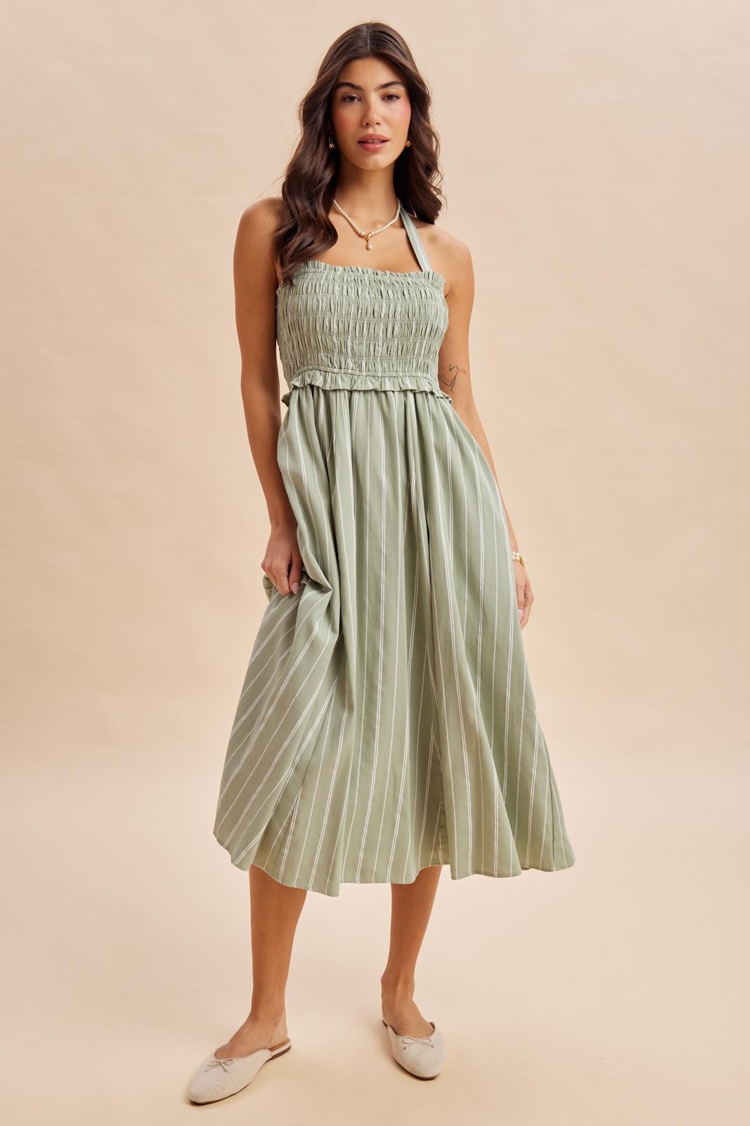 woman wearing a light green striped midi dress with a smocked bodice and halter neck