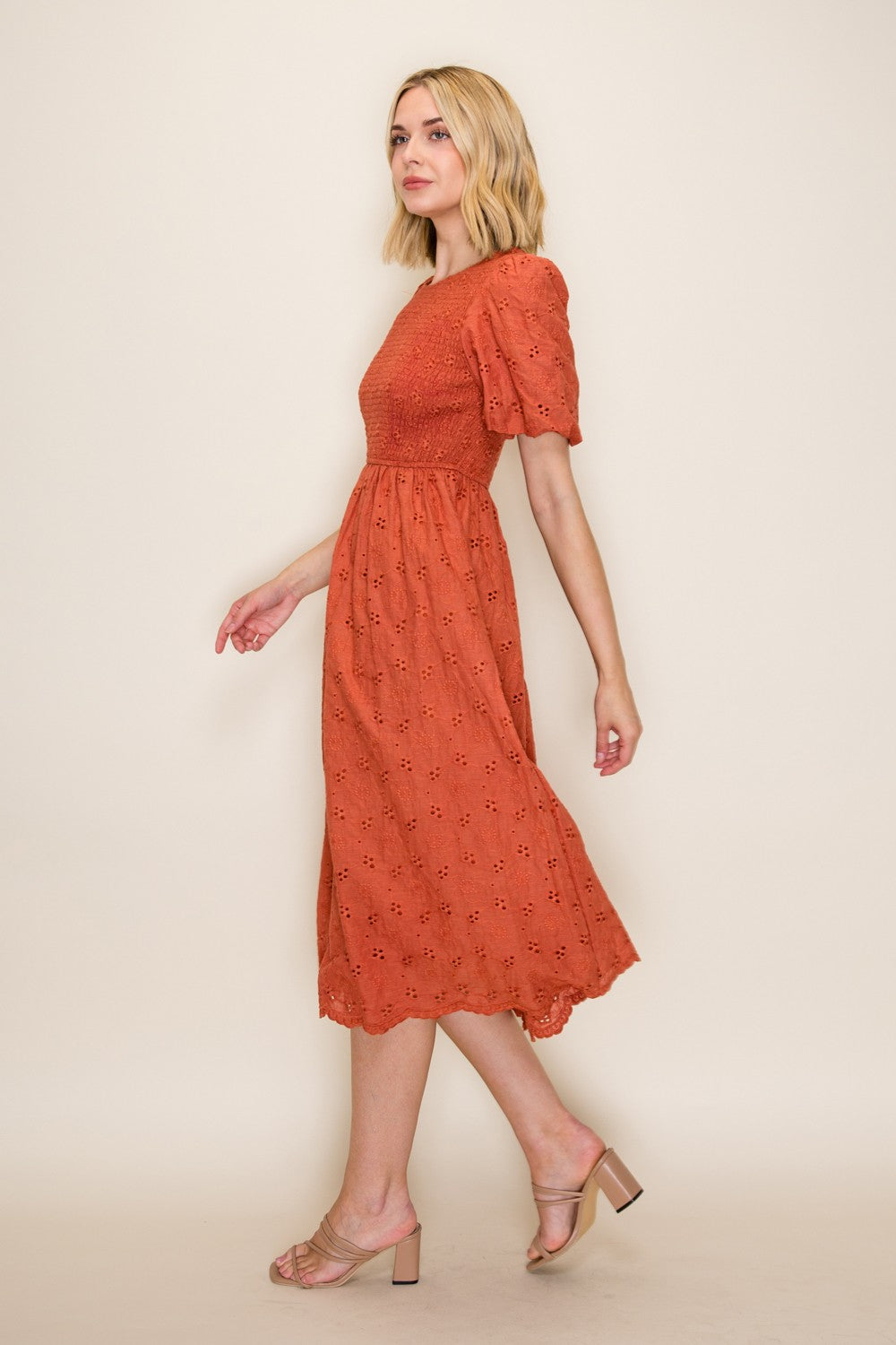 woman wearing a rust-colored midi dress with puff sleeves and eyelet details, walking gracefully