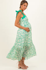 woman wearing a green and white floral maternity maxi dress with tie straps and a visible baby bump