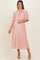 woman wearing a blush pink pleated maternity dress with a flowing cape and holding her baby bump
