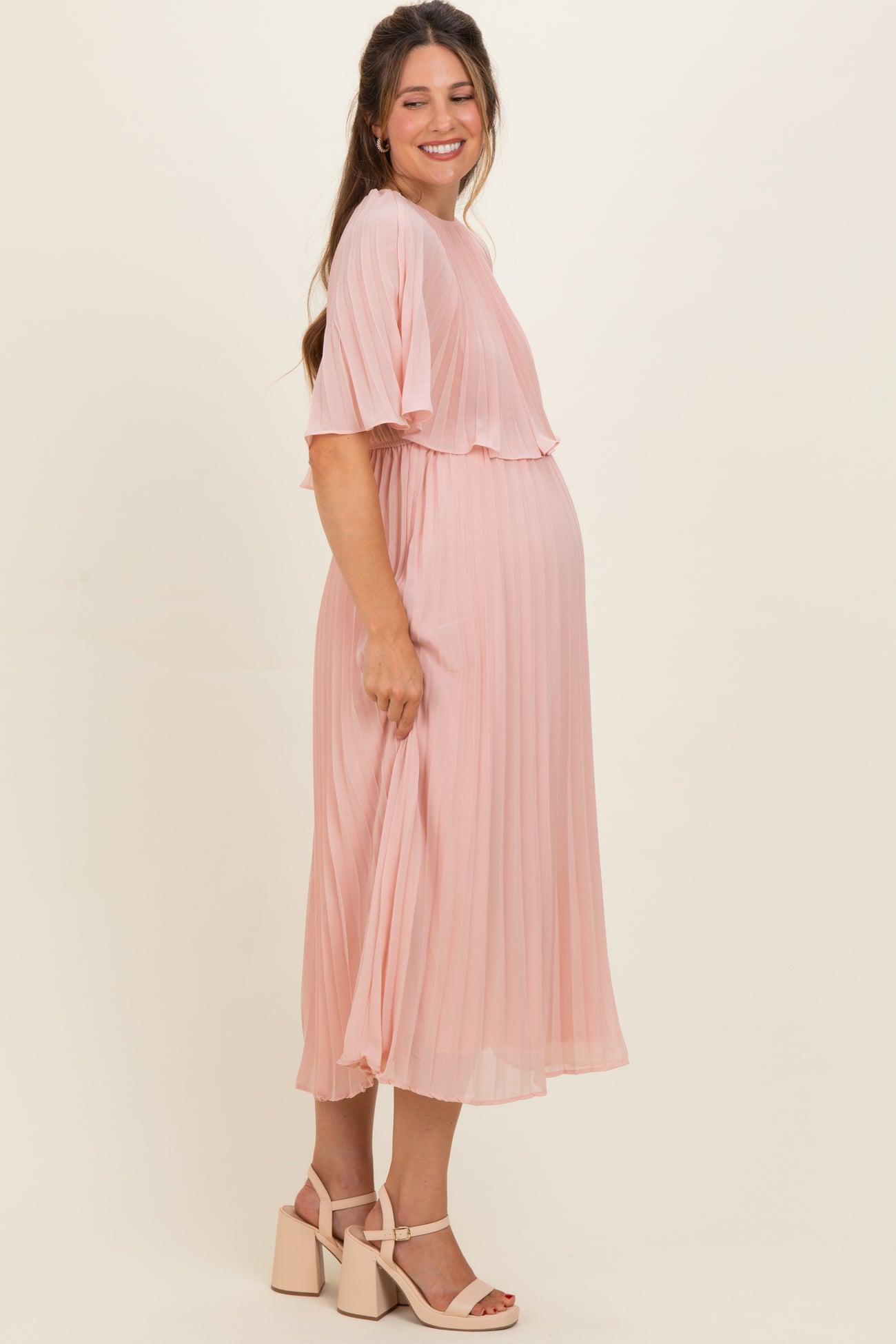 woman wearing a pink pleated maternity dress with short sleeves and a visible baby bump
