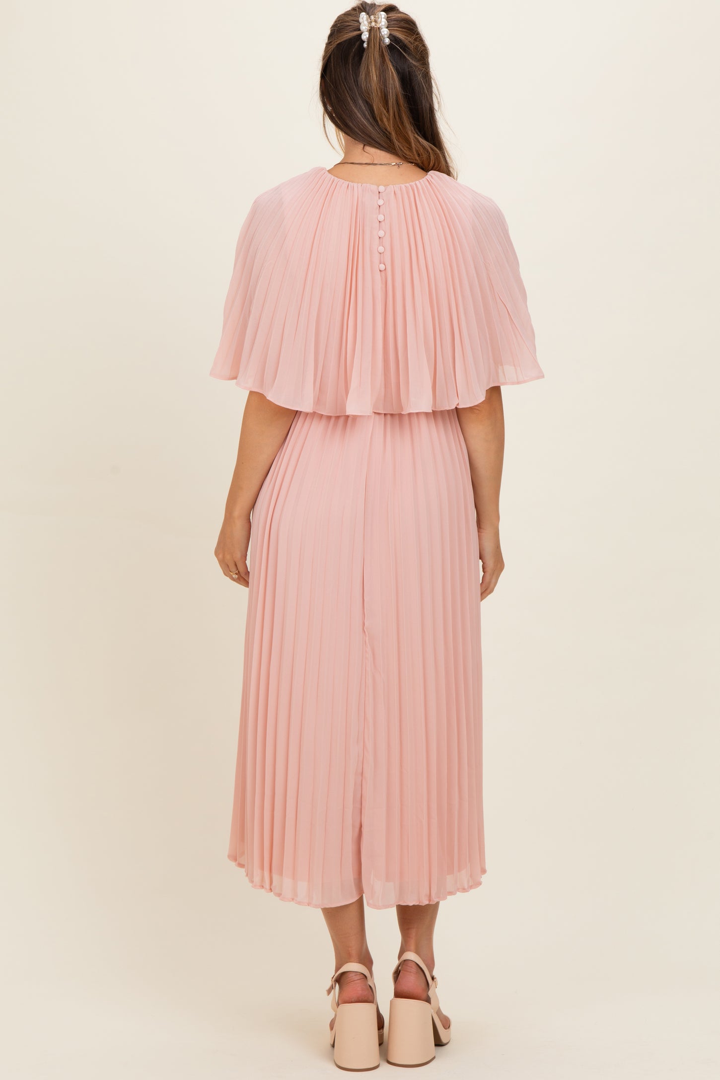 woman wearing a pleated pink maternity dress with flutter sleeves and a button detail on the back