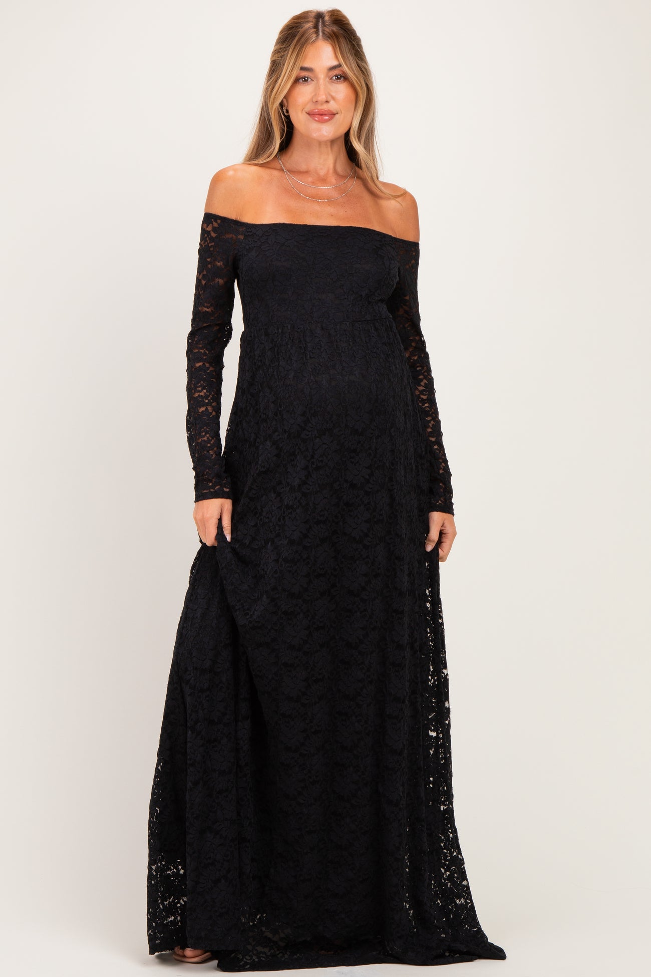 woman wearing a black lace off-the-shoulder maternity gown with long sleeves and a visible baby bump