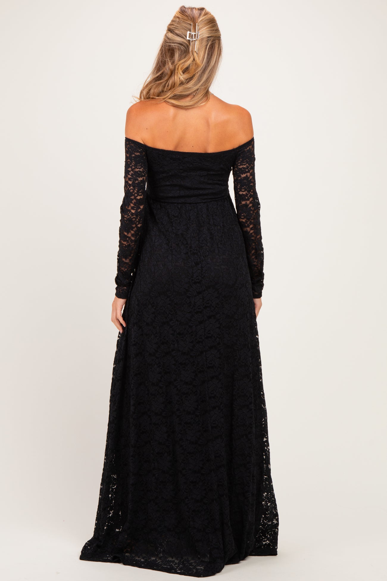 woman wearing a black off-the-shoulder lace maternity dress with long sleeves, showing a flowing maxi length and back view