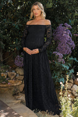 woman wearing a black off-shoulder lace maternity dress and holding her baby bump surrounded by flowers