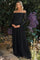 woman wearing a black off-shoulder lace maternity dress and holding her baby bump surrounded by flowers