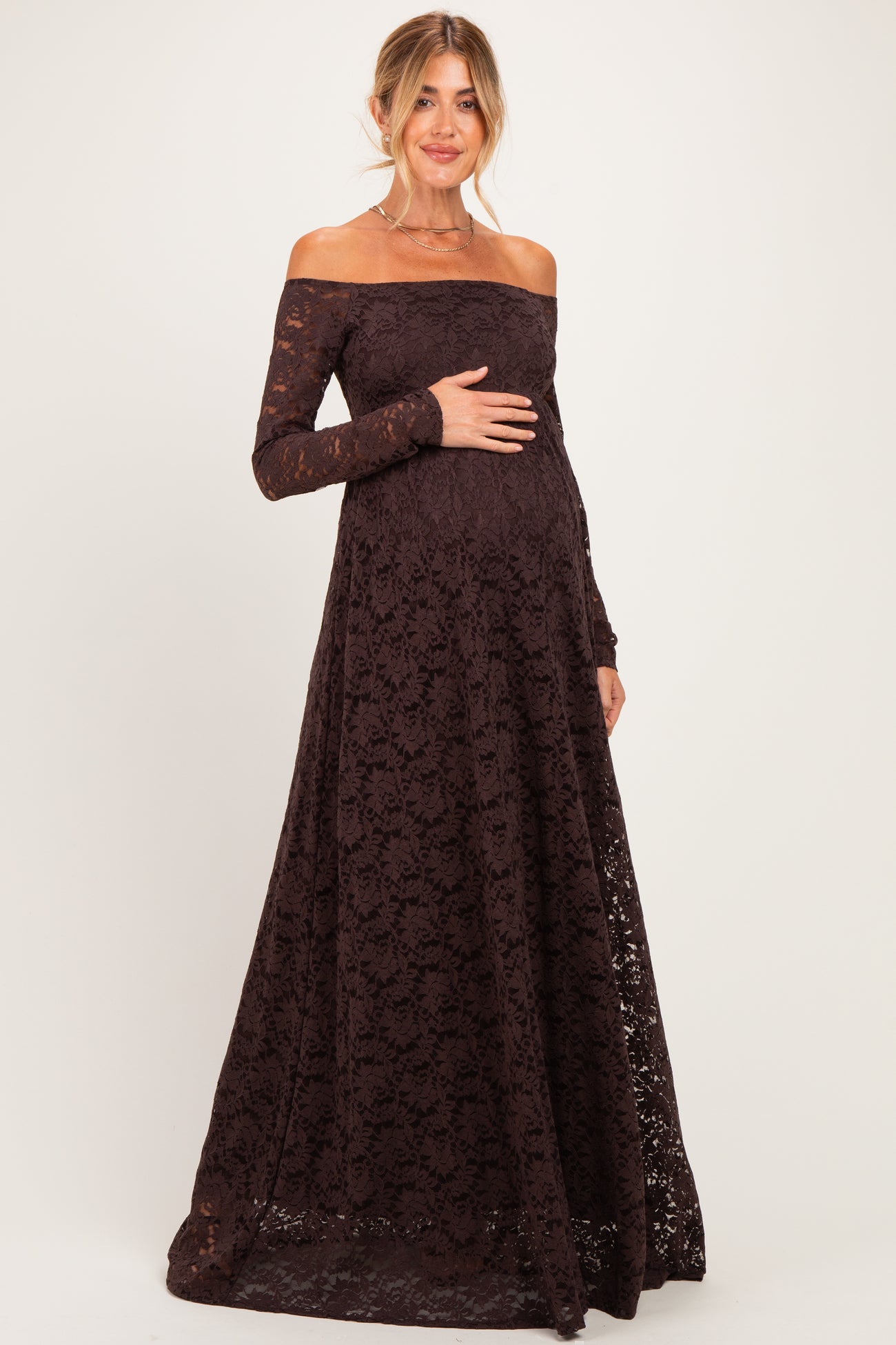 woman wearing a dark brown off-the-shoulder lace maternity gown and holding her baby bump