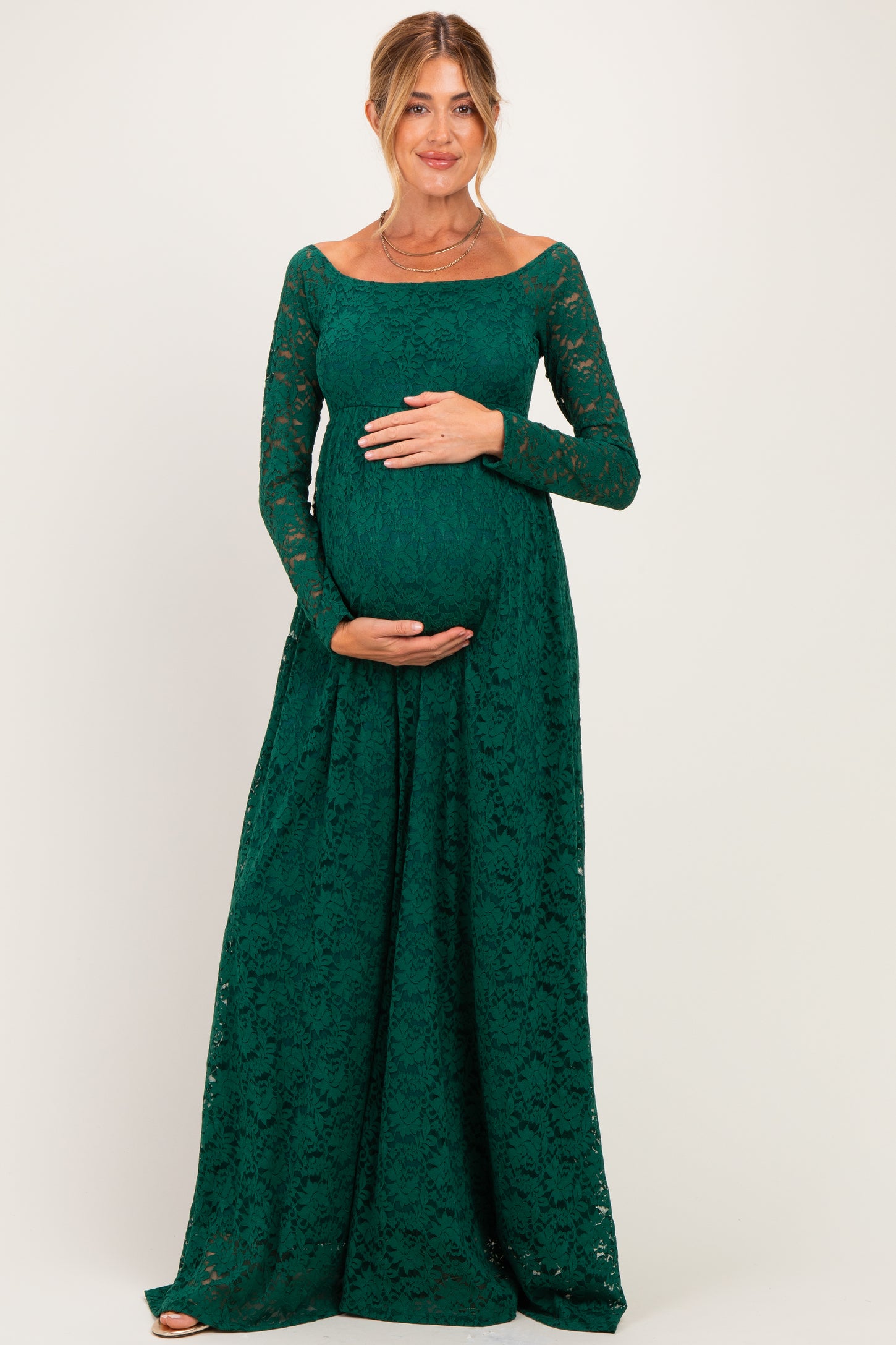woman wearing a dark green lace maternity gown with long sleeves and a visible baby bump