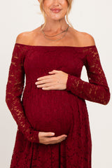 woman wearing a burgundy off-the-shoulder lace maternity dress and holding her baby bump