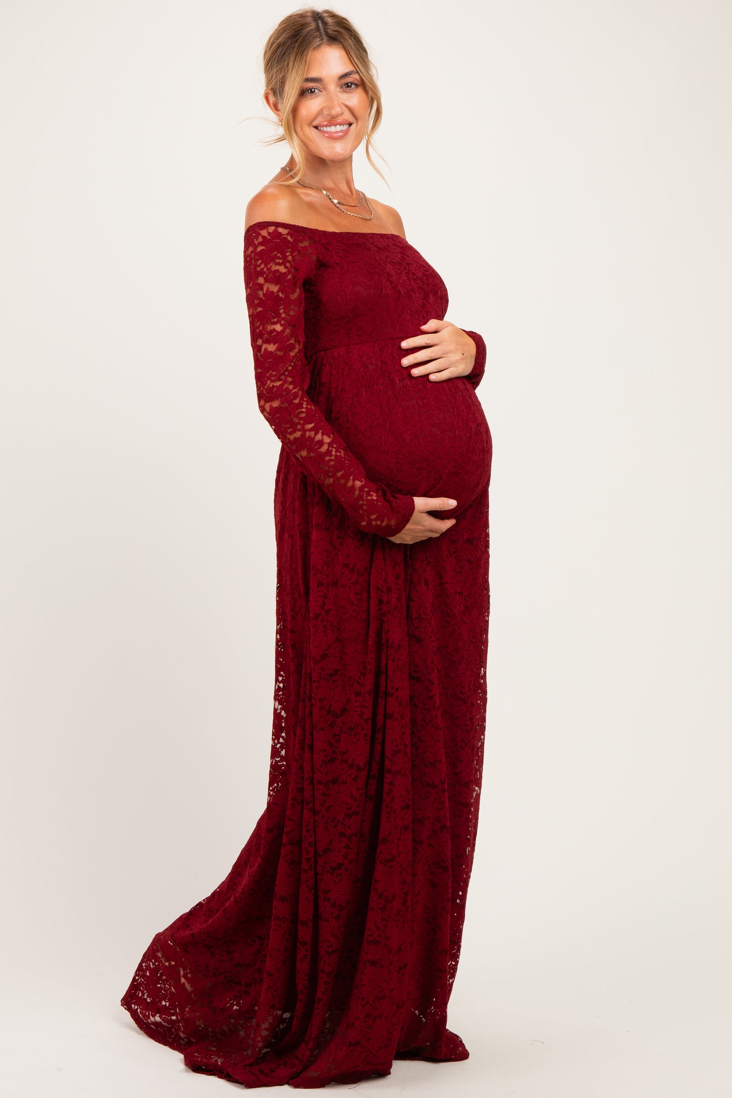 woman wearing a burgundy off-the-shoulder lace maternity dress and holding her baby bump