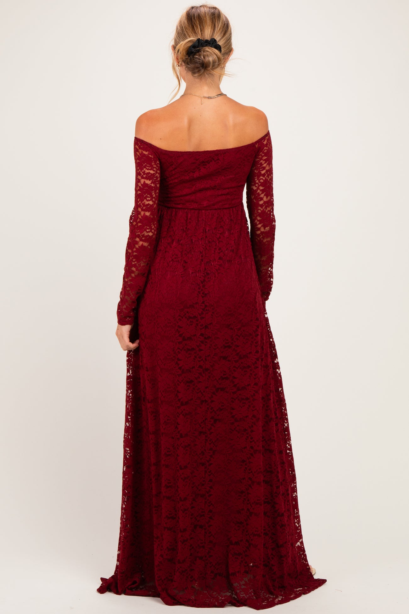woman wearing a burgundy lace off-the-shoulder maternity dress with long sleeves and a flowing skirt, showing her back