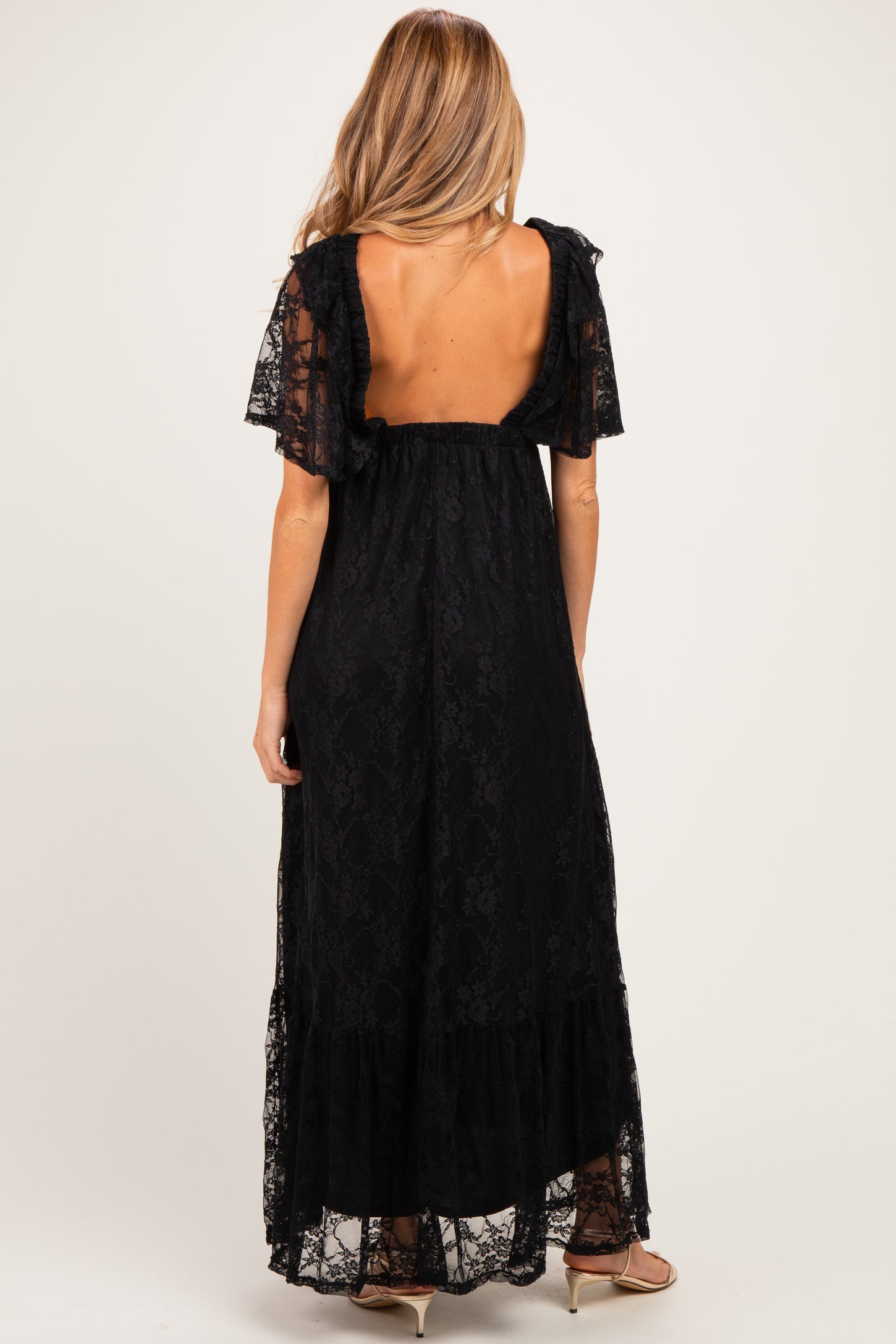 woman wearing a black lace maternity maxi dress with short flutter sleeves and an open back