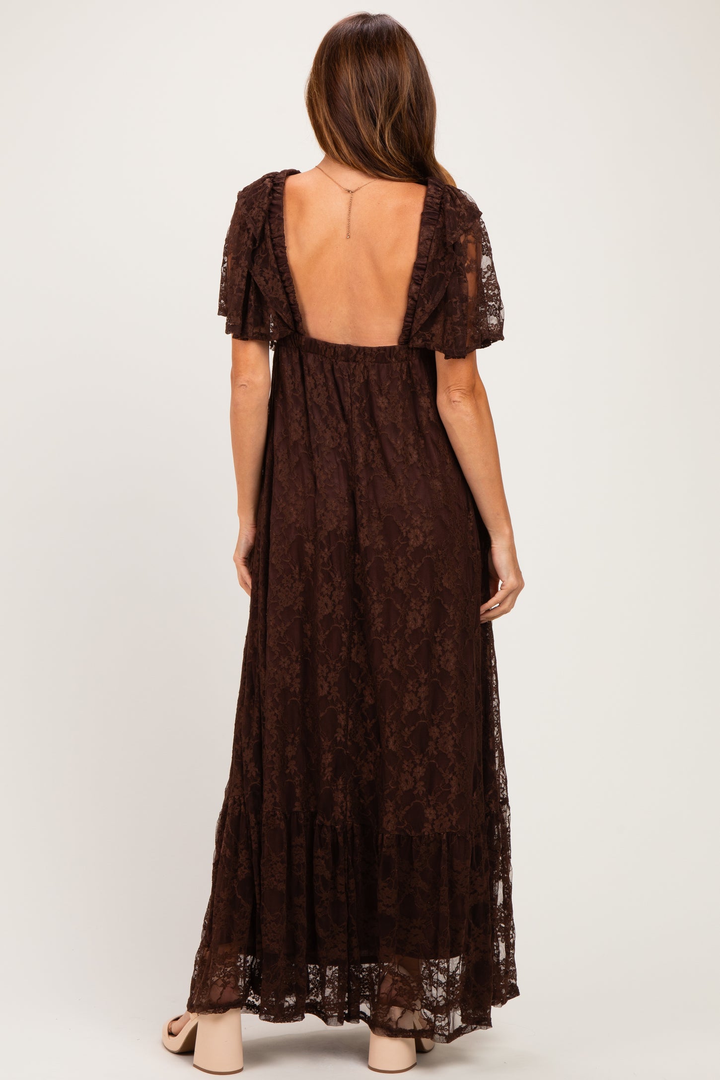 woman wearing a brown lace maxi dress with short ruffled sleeves and an open back