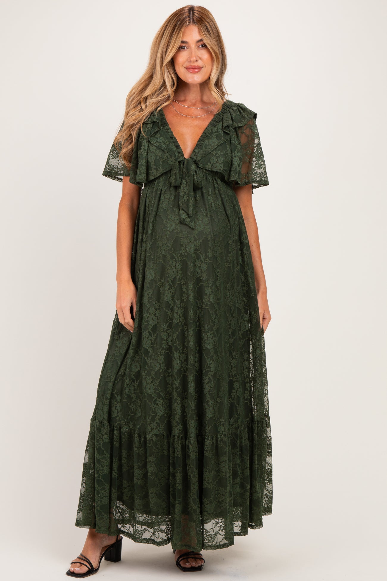 woman wearing a dark green lace maternity maxi dress with a tie detail and flutter sleeves, showing her baby bump