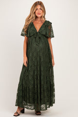 woman wearing a dark green lace maternity maxi dress with a tie detail and flutter sleeves, showing her baby bump